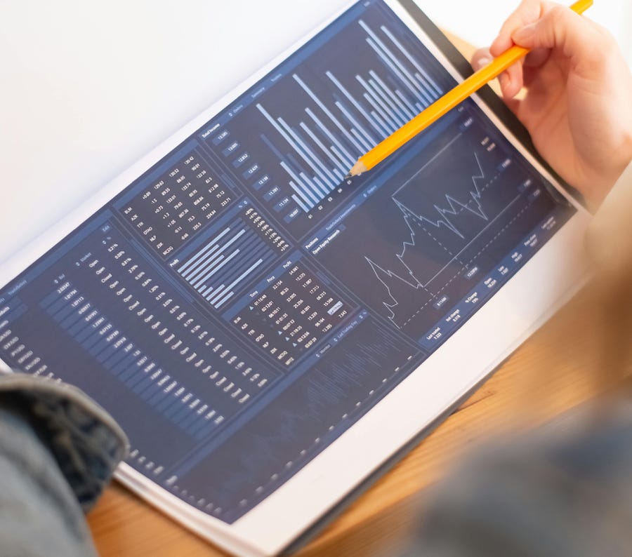 A close-up of a person analyzing blue graph data with a yellow pencil.